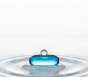 Макросъемка прозрачного стакана с водой и лежащей рядом капсулой препарата, на фоне размытых солнечных бликов